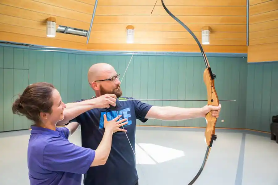 Reha-Therapie: Therapeutin trainiert Bogenschießen mit Patient Reha-Therapie: Therapeutin trainiert Bogenschießen mit Patient